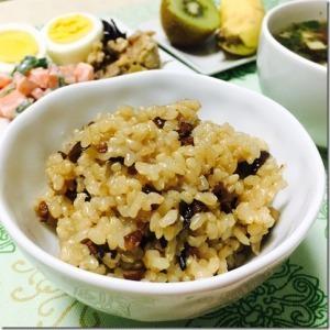 白いお茶碗に盛り付けられて玄米と黒豆を一緒に炊いたご飯と色鮮やかなおかずやデザートが並ぶ写真